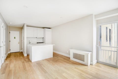 a living room and kitchen with a wood floor and white cabinets