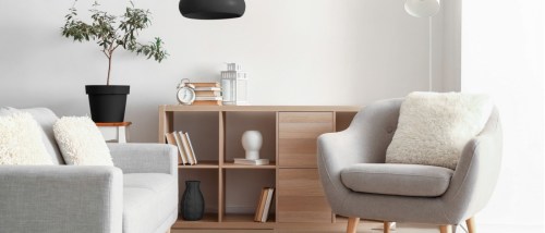 Modern living room with a cozy gray armchair, sofa, wooden shelving, and minimalist decor, illustrating the debate on furnished versus unfurnished apartments.