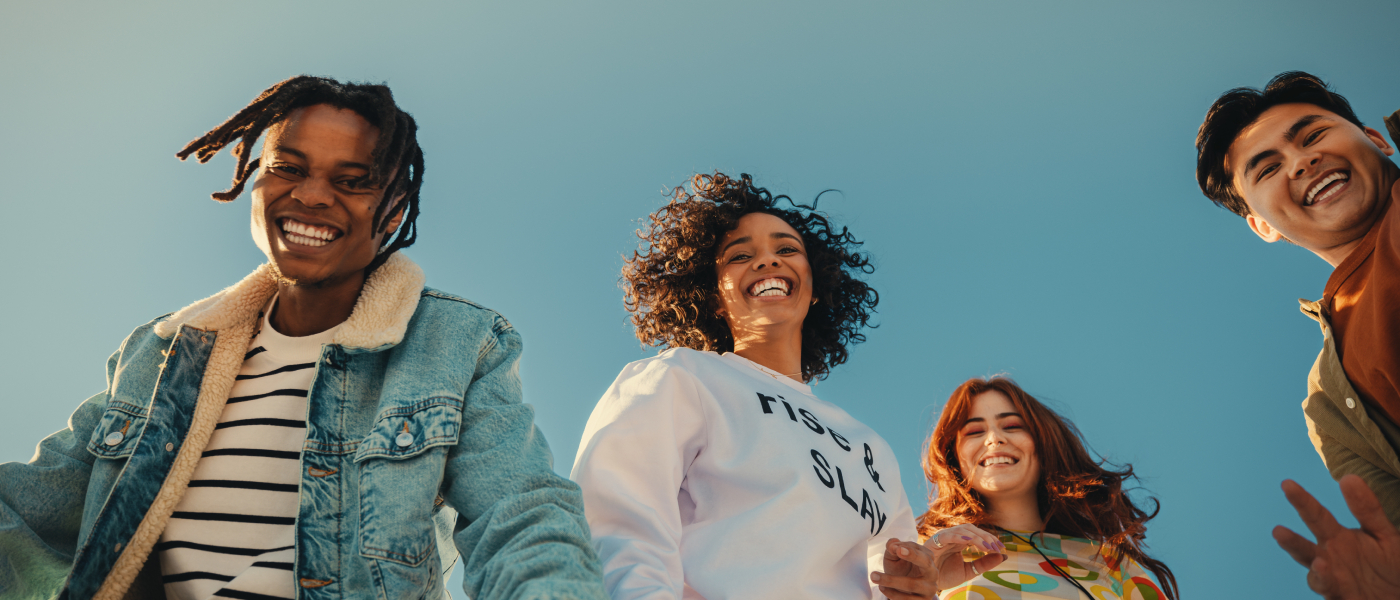 Group of smiling Gen Z friends standing under a blue sky, representing community and excitement around moving into a first apartment with a move-in checklist.