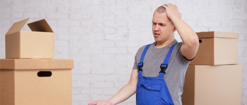 A frustrated mover in blue overalls scratching their head, surrounded by cardboard boxes, capturing the confusion of common moving day problems.
