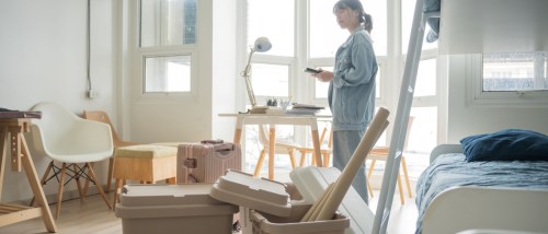 A young woman packing cardboard boxes in her apartment, preparing for relocation. Surrounded by tape, labels, and household items, she carefully organizes her belongings as part of a well-planned moving-out timeline, ensuring a smooth and stress-free transition to her new home.