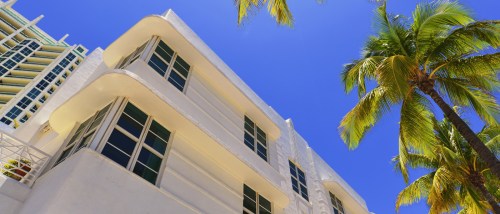 Miami apartment building with palm trees under blue sky, representing housing options and cost of living challenges for renters in the city.