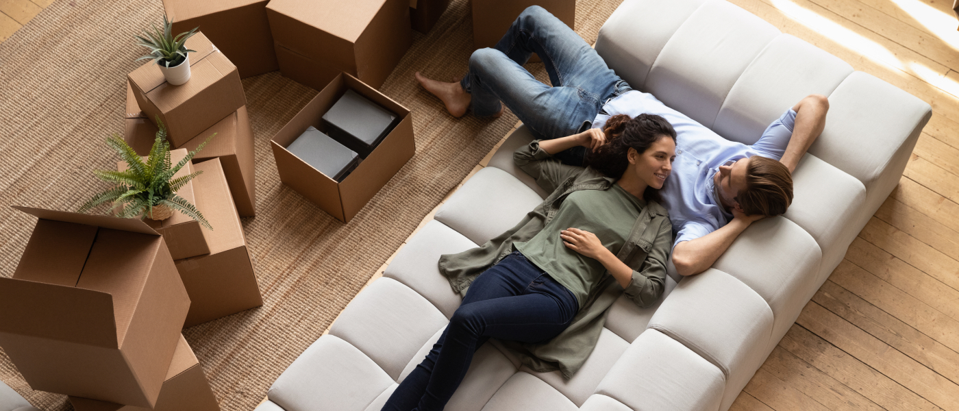 A couple sitting on a couch, surrounded by boxes, about to start settling into a new home.