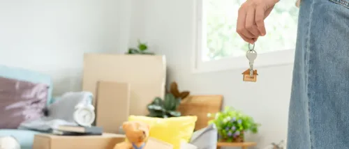 Moving house, relocation. Woman holds key with house keychain in new apartment.