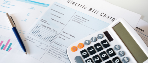 Bills for an apartment with utilities included, including gas and electric charges, alongside a calculator and pen on a white desk.